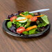 A plate of salad with a black velvet paper plate and a fork.