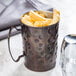 A World Tableware hammered antique copper Moscow Mule mug filled with french fries on a table.