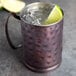 A World Tableware hammered antique copper Moscow mule mug filled with ice and a lime wedge.