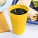 A School Bus Yellow plastic cup filled with a yellow liquid and ice on a white background.