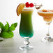 Two glasses of colorful drinks garnished with Tablecraft bamboo cocktail picks, one with an orange slice.