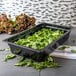 A Carlisle black plastic food pan filled with spinach on a counter.