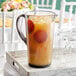 A Carlisle smoke Tritan plastic pitcher of orange juice with ice and orange slices on a tray.