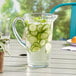 A Carlisle Tritan plastic pitcher of water with cucumbers and mint on a table.