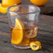 A Carlisle clear plastic double rocks glass with liquid, ice, and a slice of orange.