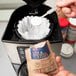 A hand holding a white packet of Urnex coffee and tea urn cleaning powder.