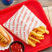 A red tray of Carnival King extra large French fry bags with a hot dog and fries on it.