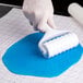 A hand using a Wilton Dot Pattern roller to emboss blue fondant.