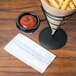 A white dispenser napkin on a table next to a black metal container of french fries.