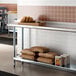 A Regency stainless steel work table with a shelf holding brown bags and bread.