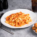 A Tuxton oval china platter with a plate of pasta with sauce and a drink on it.
