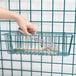 A hand using a wire whisk to stir a metal tube in a basket.