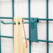 A green metal hook with a wooden spoon hanging from a wooden peg on a Metro SmartWall.