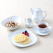 A white Tuxton round china cup filled with brown liquid on a saucer with a waffle and berries.