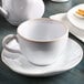 A Tuxton white china saucer with a white cup on a table.