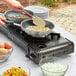 A person using a Choice portable gas stove to cook eggs in a pan.