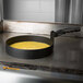 A Prince Castle black non-stick egg ring in a pan with yellow liquid cooking in it.
