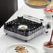 A Chef Master portable butane gas countertop range with a flame cooking food in a pan on a table.