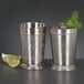 Two World Tableware stainless steel mint julep cups filled with ice and mint next to a lime wedge.