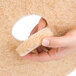 A close-up of a hand holding a 3M tan round floor pad.