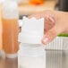 A hand using a white Tablecraft triple tipped cap to pour from a plastic bottle.