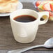 A tan stackable melamine cup filled with coffee on a saucer with a spoon.