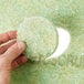 A hand holding a round green 3M TopLine Autoscrubber floor pad with a hole in it.