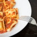 A white deep coupe bone china plate with ravioli and sauce with a fork.