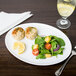 An oval white porcelain platter with a plate of food and a slice of lemon.