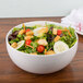 An Arcoroc white porcelain bowl filled with salad, cucumbers, and tomatoes.