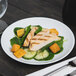 An Arcoroc white porcelain salad plate with a chicken and spinach salad on a table.