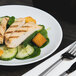 A white Arcoroc porcelain salad plate with chicken and spinach salad and a fork.