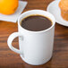 A white porcelain Arcoroc mug filled with coffee on a table.