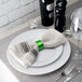 A white plate with a Tabletop Classics by Walco Forest Green napkin ring on a table with silverware and a glass.