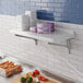 A Cambro Camshelving® wall shelf above a counter with food on it.