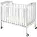 A white L.A. Baby mini wood crib with wheels.