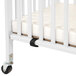 A white L.A. Baby mini wood crib with wheels.