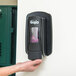 A person's hand using a black GOJO manual soap dispenser.