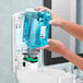 A person's hands pouring blue GOJO foaming hand soap into a dispenser.