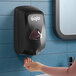 A black GOJO TFX 1200 mL touchless hand soap dispenser mounted on a blue tiled wall.
