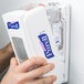 A hand using Purell hand sanitizer on a wall-mounted Purell dispenser.