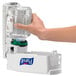 A hand holding a clear bottle of Purell foaming hand sanitizer in front of a Purell dispenser.