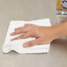 A hand using a white Carlisle microfiber cleaning cloth to wipe a table.