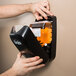 A hand holding a black GOJO TFX soap dispenser with a bottle of GOJO Fresh Fruit Foaming Antibacterial Hand Soap