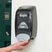 A person using a black GOJO manual hand soap dispenser.