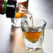 A person pouring liquid into an Anchor Hocking shot glass on a table.