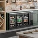 A black counter height glass door pass through back bar refrigerator filled with assorted beverages.