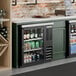 A black counter height glass door back bar refrigerator filled with assorted beverages.