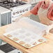 A woman holding a Vollrath bun / sheet pan cover over a tray of cookies.