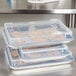 A stack of three clear plastic Vollrath bun pan covers with cookies in them.